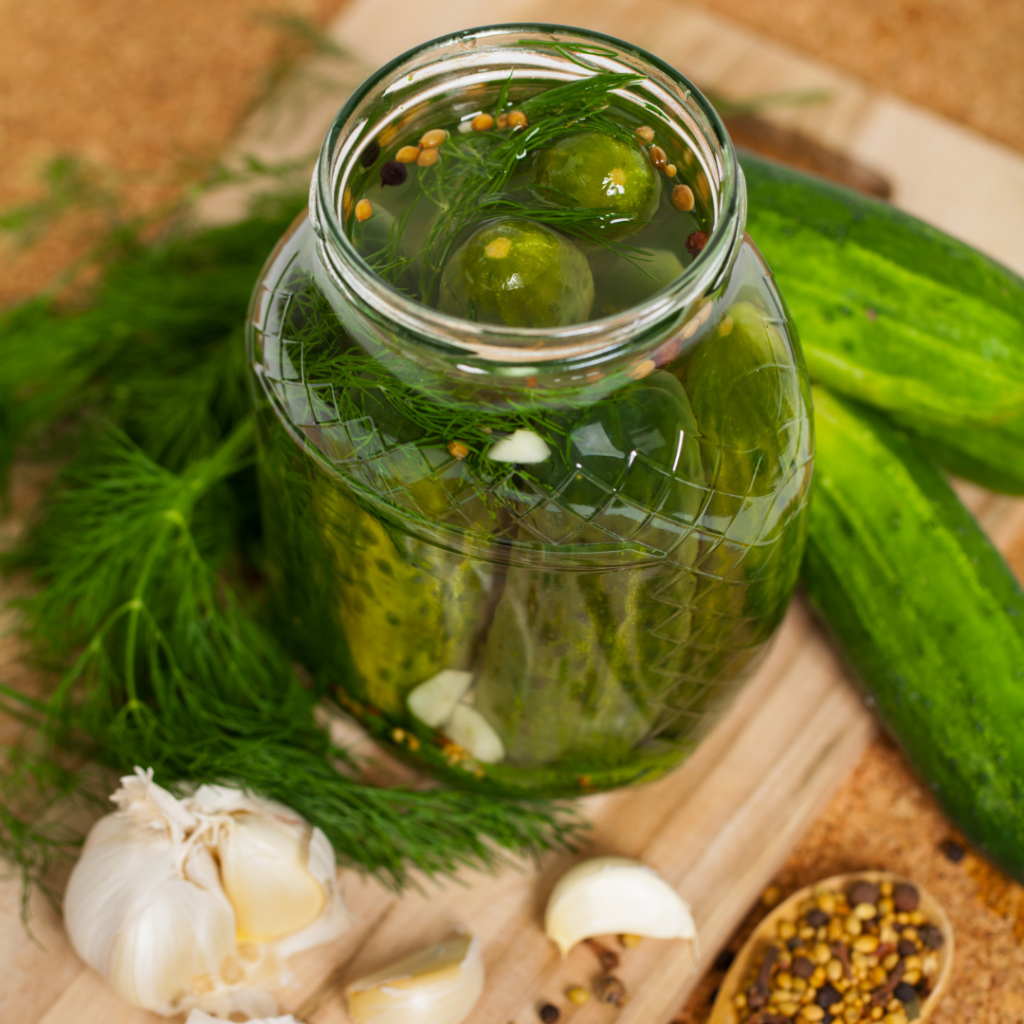 Pickles in a jar with dill, garlic and spices surrounding the jar.