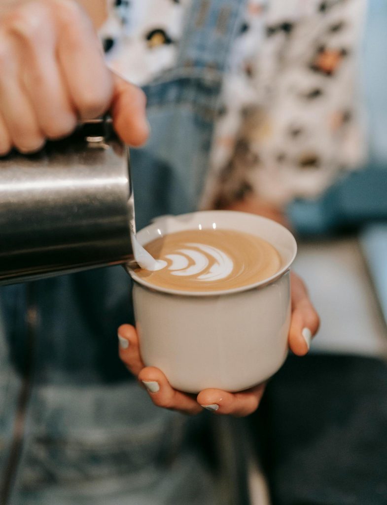 Woman holding a cup of coffee while poring creamer in.